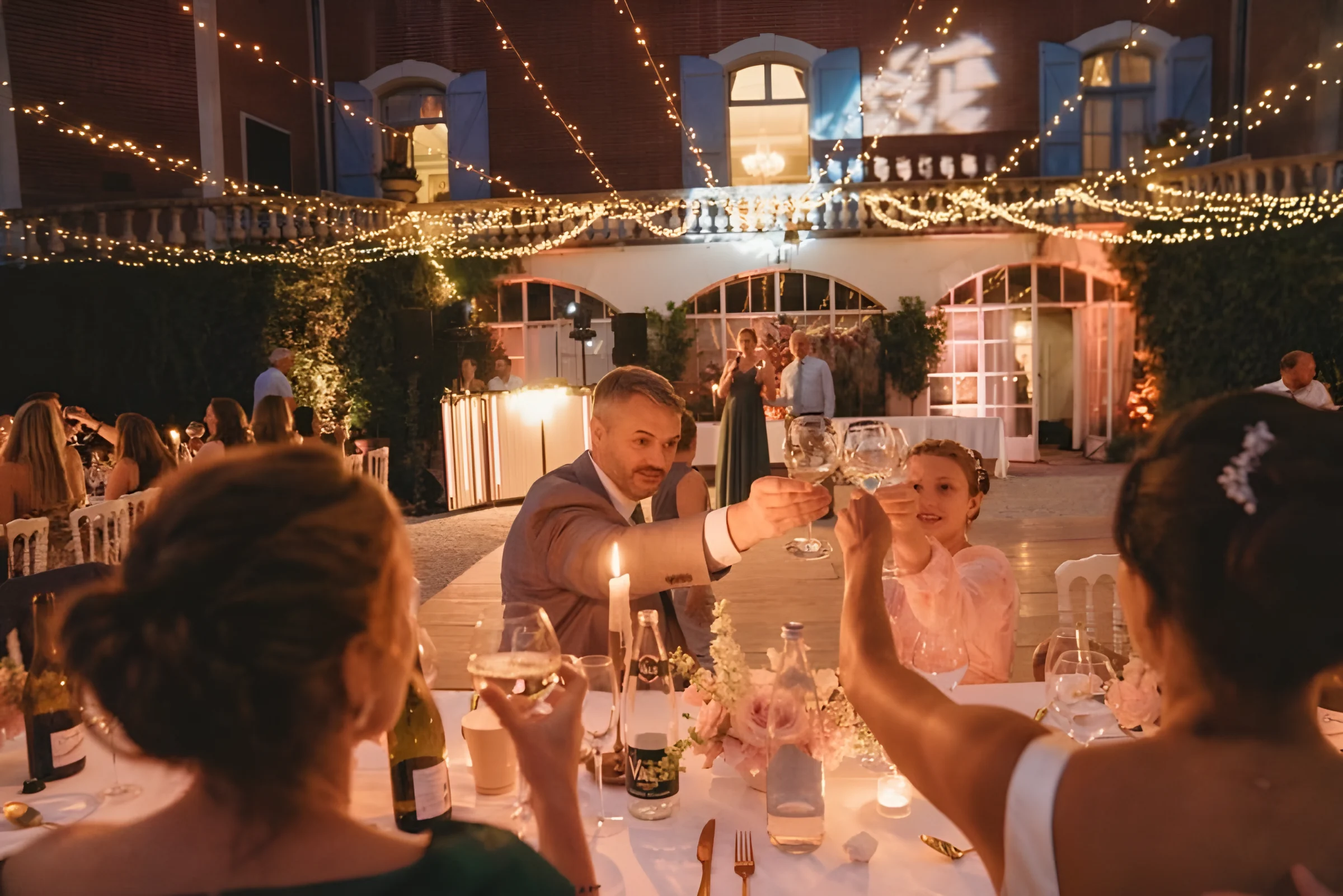 Guests raising their glasses at a candlelit dinner beneath strings of lights at Château de Garrevaques